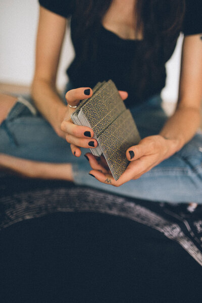 Miranda shuffling a deck of tarot cards with intricate patterns, seated cross-legged on a dark tarot cloth, creating a mystical and reflective atmosphere.