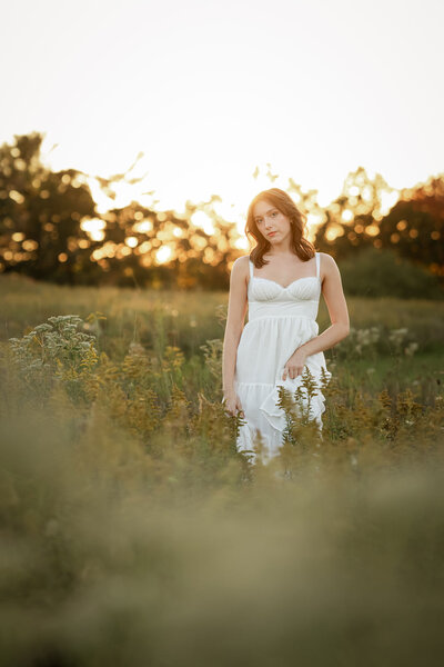 A high school senior stands in a field during golden hour in Pittsburgh, bathed in warm, glowing sunlight. The soft light highlights their natural beauty as they smile, capturing a serene and reflective moment in nature.