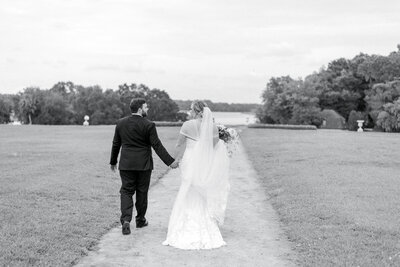 black and white portrait of bride and groom walking and holding hands on the path in the butterfly gardens at middleton place in Charleston South Carolina