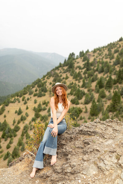 A young woman sitting on the side of a mountain while crossing her arms on her legs.