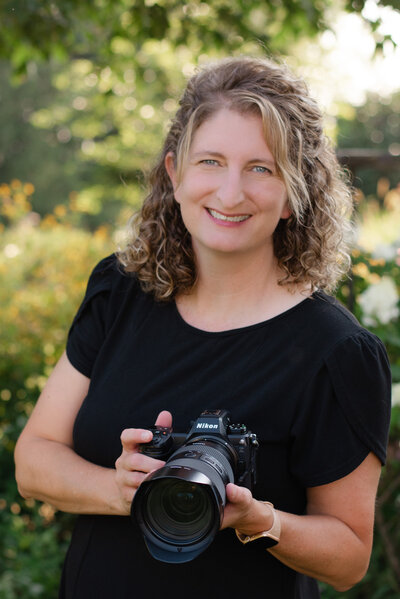 Heather smiling in a black shirt while holding a camera