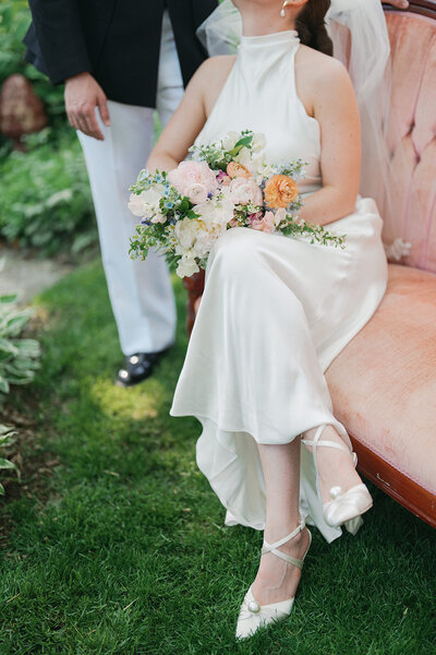 a close up of a bridal bouquet on the lap of a bride sitting on a peach colored couch.
