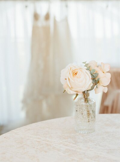 wedding flowers with wedding dress hanging in the background