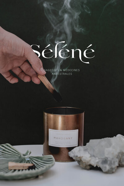 Main brûlant du palo santo au dessus d'une bougie en métal bronze. Ceramique verte en forme de coquillage et roche semi-précieuse devant. Logo Séléné incrusté en fond.