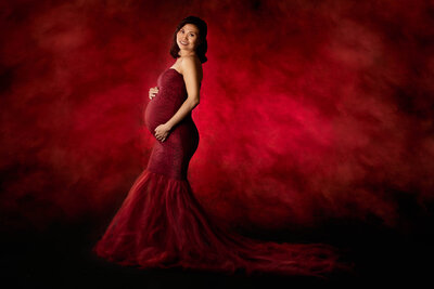 Elegant studio maternity portrait featuring an expectant mother in a stunning red gown against a dramatic backdrop, captured in Overland Park, Kansas. A timeless choice for artistic maternity photography in the Kansas City metro area.