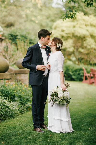 bride and groom kiss while holding a lgass of champagne