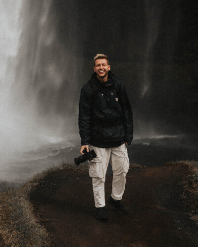 Man standing in front of a waterfall holding a camera