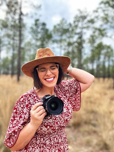 Portrait of Nikki Rinc, a Florida-based wedding and family photographer with Salt + Heart Photography, smiling with a Nikon camera in a natural field setting