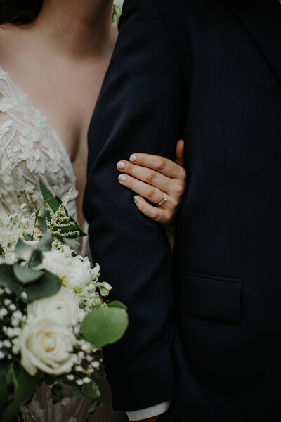 Bride holding onto Groom's arm with ring hand showing color palette and bouquet details