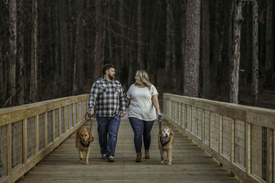 Engaged couple look at one another while their two Golden Retrievers lay at their feet