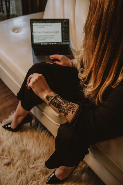 A blonde woman with a tattoo on her forearm is looking at a laptop screen that shows various font selections.