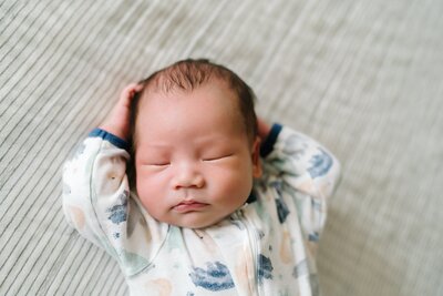 Sleeping newborn baby with arms by his head, laying on master bed during Shoreline, WA newborn portrait session