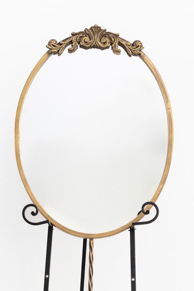 Gold oval mirror with ornate decorative top on black easel stand