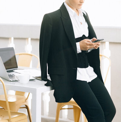 Female entrepreneur texting in a black and white suit.