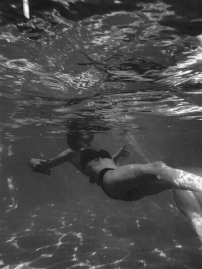 A woman gracefully swimming underwater in a black bikini, captured in motion with the light filtering through the water, illustrating fluidity and freedom.