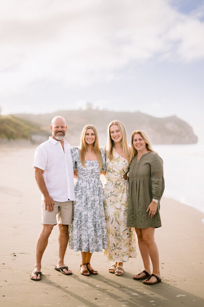 High school senior girl with long brown hair wearing a white dress, smiling by a lifeguard tower at Pismo Beach during her senior photo session with Rosa Clark Photography.