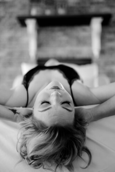 boudoir pose of woman laying on her back with her hands behind her head and her back arched at little rock boudoir studio