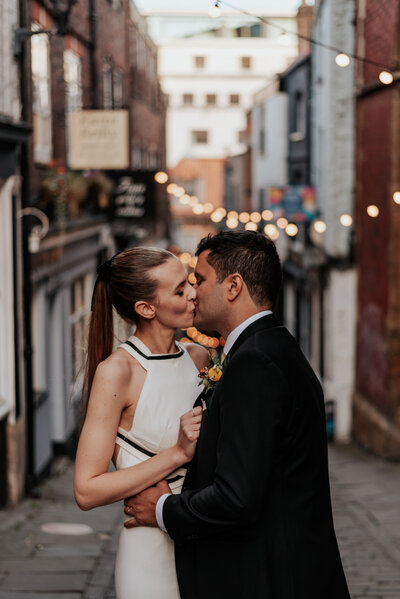 Bride and groom kissing  with festoon lights behind them on the Christmas Steps in Bristol