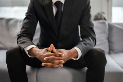 A businessman dressed in a dark suit and tie, sitting with hands clasped together, exuding a poised and confident demeanor.