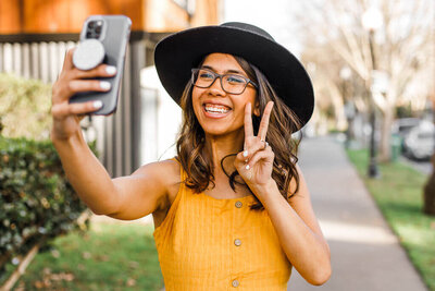 woman holding up peace sign at phone