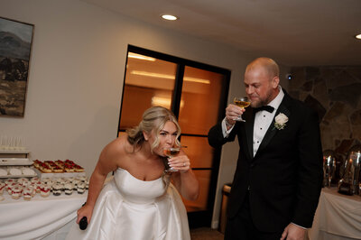 Wearing all white, a woman leans against a concrete wall in downtown Raleigh with her fiancé to her side. He is also leaning against the wall, looking at her.