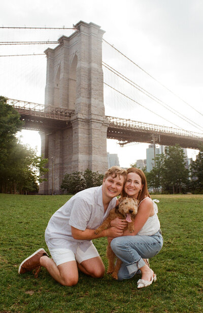 couple posing with dog in front of brooklyn bridge