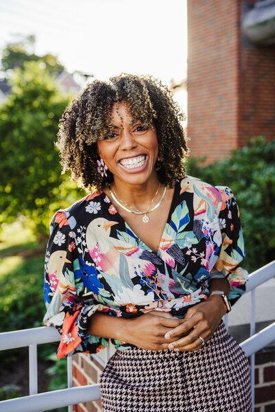 woman in black turtleneck smiles against a brick wall for headshot