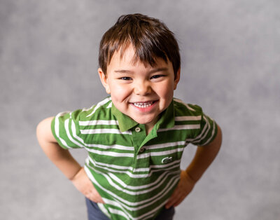 A little boy peeks playfully over his pulled up shirt collar during his school picture day with Kate Simpson Photography.