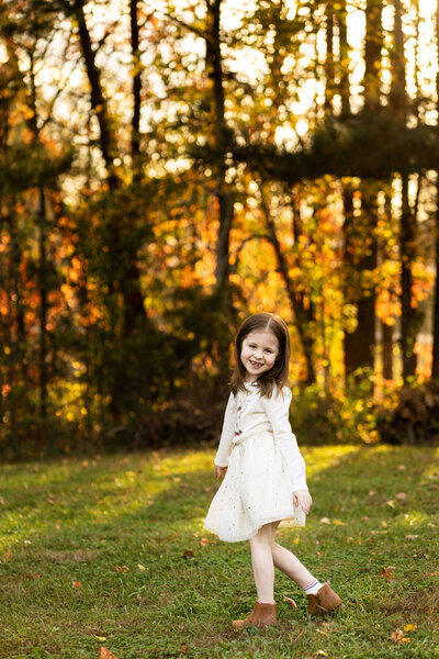 Young girl smiling at the camera with fall foliage in the background