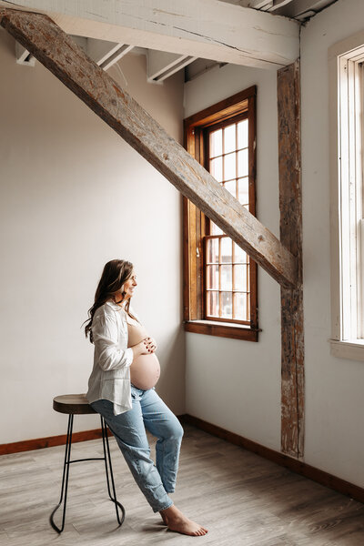 Pregnant woman sitting on stool looking out window holding belly