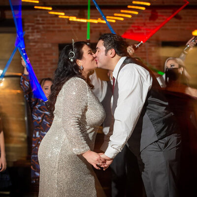 wedding couple kisses in front of colored lights
