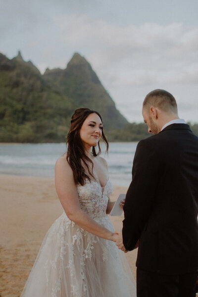 Bride smiles at groom while he reads vows to her in Kauai