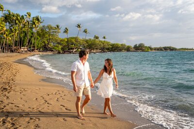 Couple walking barefoot along the shore at ʻAnaehoʻomalu Bay in Waikoloa after a surprise proposal, photographed by Hawaii Adventure Portraits, a Big Island proposal photographer