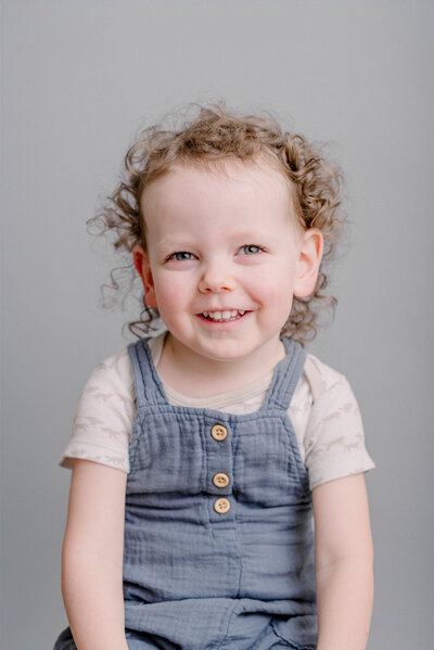 A little boy sits for his school portraits against a gray backdrop with a beautiful modern style.