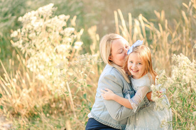 Mom in a denim jacket hugging her young daughter in a field of yellow grass
