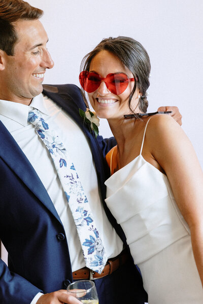 groom lovingly looking at bride with pink heart sunglasses on