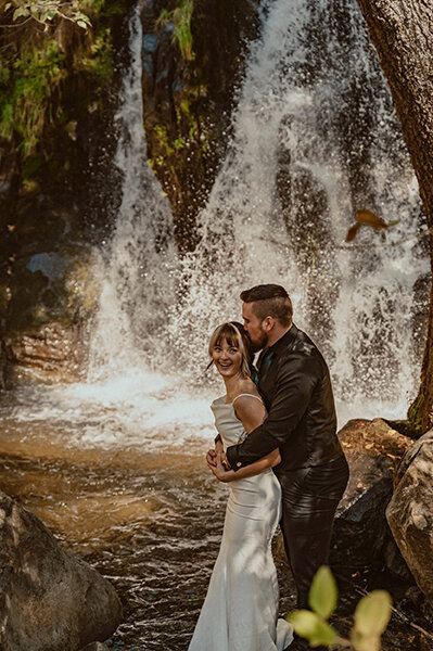 bride and groom embracing underneath a secret waterfall near yosemite national park