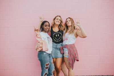 three woman against a pink brick wall