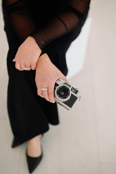 Detail photo of photographer Kelly Lugo wearing elegant black dress and holding Holga film camera