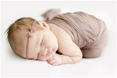 close up of baby girl on belly snuggled in wrap with a bow headband by Charlotte Newborn Photographer