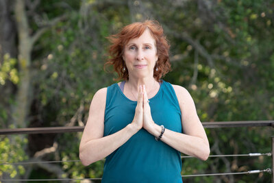 Woman standing outside in a simple, welcoming yoga pose, smiling.