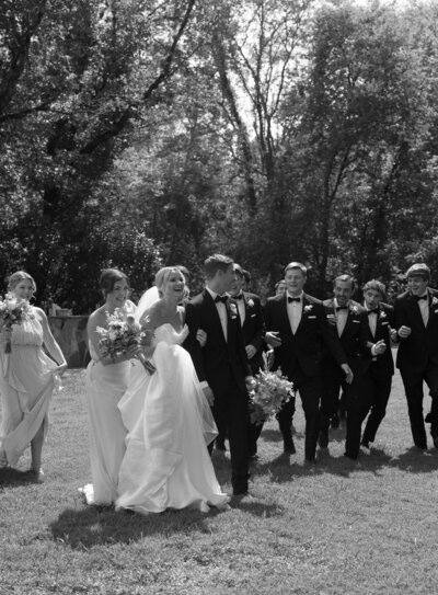 Black and white photo of a wedding party walking together while laughing.