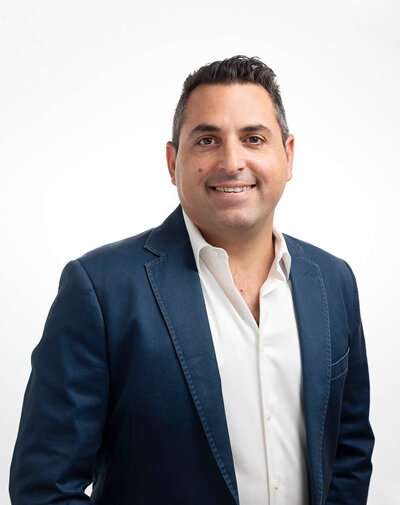 CEO of large company is posing with a blue blazer over white backdrop for his professional headshot taken by Ingrid Barnhart Photography in Austin