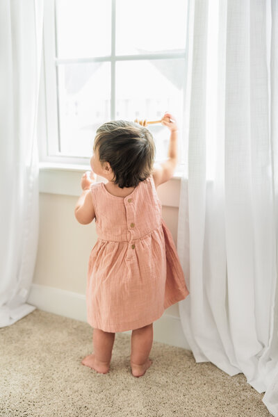 A toddler gazing out the window, softly lit by natural light.