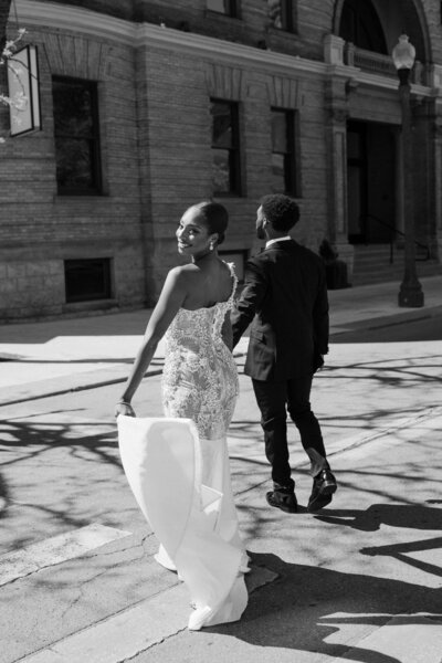 A newlywed couple holding hands and walking across the street 