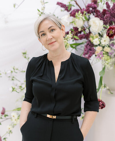 Carmel smiling in front of a lush pillar of pink and deep red flowers at Stonehaven.