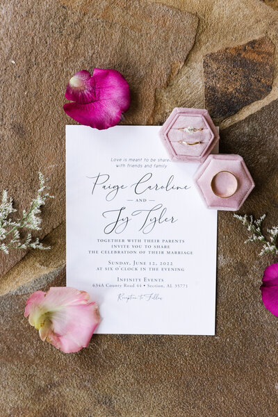 Wedding rings are artfully stacked atop a cream and gold wedding invitation