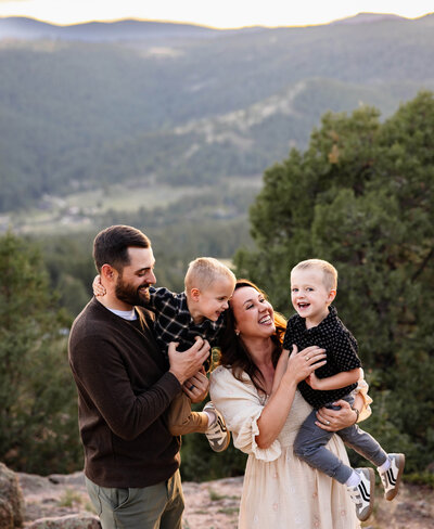 A family with twin boys hold them and laughs during their family photo session at Mt. Falcon Park in Jefferson County, Colorado.