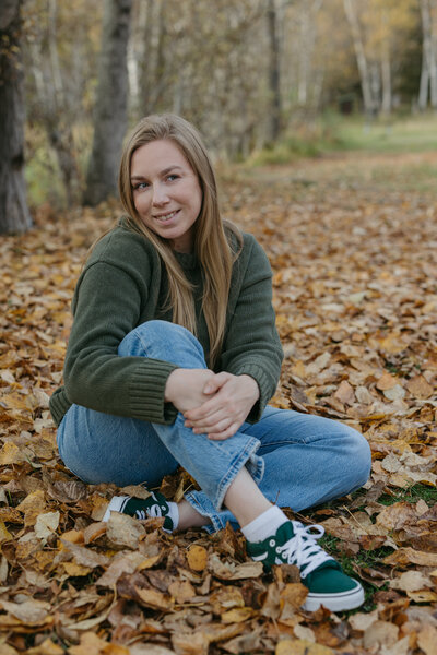 A woman sitting on the ground wearing blue jeans and a green sweater.