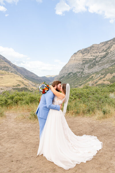 Soon to be bride and groom share a kiss amongst a beautiful backdrop of mountains and blue skies.